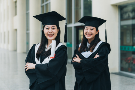 Young asian women students wearing graduation cap and uniform with crossed arms looking at the camera.の写真素材