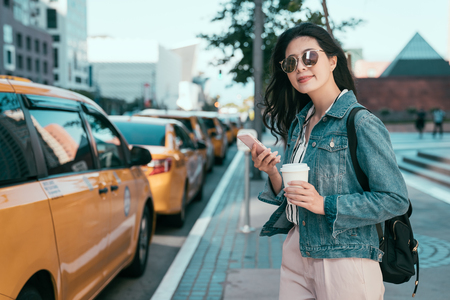 confident business woman using application of taxi service app on smart phone and holding coffee to go.の写真素材