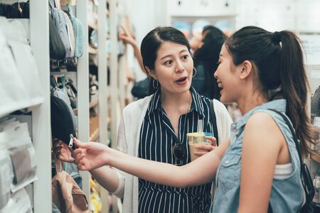 Two smiling female friends selecting products in grocery store. young girls discussing about summer trip to usa buying pillow bag on shelf hold look. happy asian women talking laugh in shop hong kongの写真素材