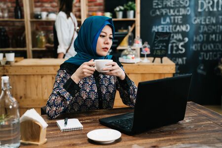 arabic businesswoman drinking tea and using laptop  in coffee shop.の写真素材