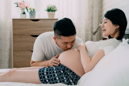 Pregnant couple hugging and kissing at home in bedroom. young handsome asian chinese husband and...