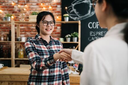 friendly asian woman recruiter standing at cafe bar table shaking hands with applicant just arrived for interview. hr managers greeting candidate nice to meet you good first impression in coffee shopの写真素材