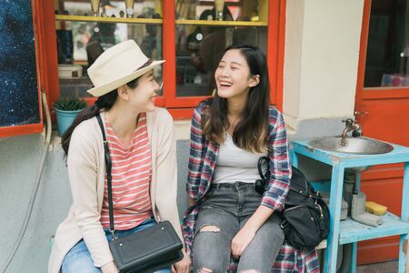 Happy female best friends relax outdoor of small shop while visiting small village.の写真素材