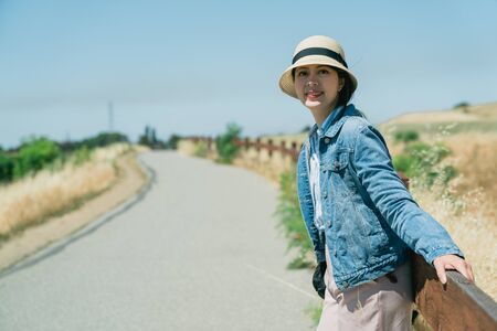 Happy attractive asian japanese woman hiker leaning on a rustic wooden fence while contemplating view in alpine green pastures.の写真素材