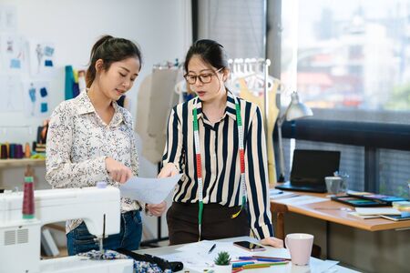 Two asian japanese female fashion designer coworkers creatives discussing magazine layout in office.の写真素材
