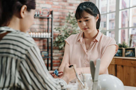 Gorgeous young asian korean woman getting her nails done by manicurist in spa salon. smiling office lady worker after work doing manicure in beauty workshop. beautician painting nail polish on clientの写真素材