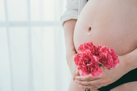 close up portrait of asian korean pregnant woman bare belly and holding flower isolated on white...