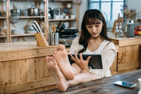 On the weekend, a woman is watching an online movie and sitting relaxed on the wooden chair and table.の写真素材