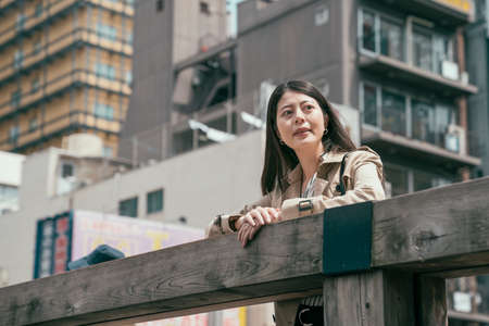 beautiful young asian japanese woman in stylish coat leaning on handrails and smiling while standing...
