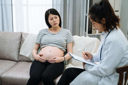young asian korean pregnant woman sitting on sofa during psychotherapy. Worried maternity lady...