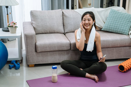 sport technology and healthy lifestyle concept. smiling asian chinese woman in wireless earphones listening to music on smartphone at home living room. fitness young girl in headphones.の写真素材
