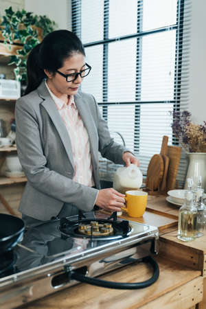 asian career woman is feeling thirsty and filling mug with milk in a peaceful morning. chinese female lady standing in her kitchen is having her daily milk before going to work.の写真素材
