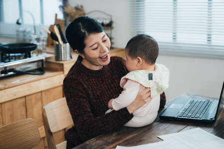 portrait happy asian freelancer mother is looking and playing with her baby girl while working from...