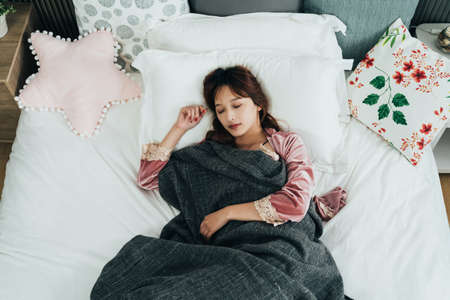 view from top beautiful asian girl under cover is sleeping soundly alone in white bed on a tranquil morning at a bright home bedroom.の写真素材