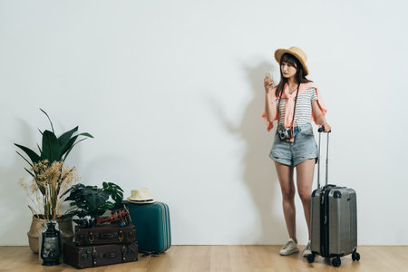 full length lost asian woman carrying a luggage in summer casual wear is using gps app on the phone for directions with isolated white wall background.の写真素材