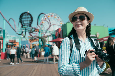 Photographer girl with lens camera. woman tourist enjoy summer vacation outdoors takes pictures in amusement park. joyful female professional photographer relax with bokeh view ferris wheel in backの写真素材