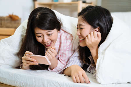 Young attractive asian chinese female in white bed cover by warm blanket. girl friends wearing...