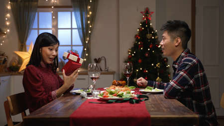 side view of excited asian woman looking into gift box and screaming in surprise while her boyfriend...