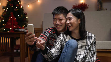 asian man and woman in love are sitting close and enjoying watching online video on the smartphone...