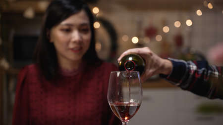 selective focus of a Japanese maleâs hand serving and swirling wine in the wineglasses while his wife is looking on blurred background at the indoor romantic dinner dateの写真素材