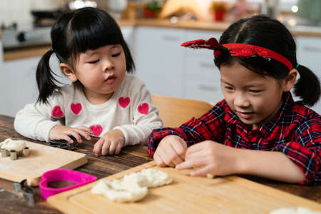 closeup of an innocent Taiwanese baby girl looking at her sister shaping dough with curiosity while baking Christmas cookies in the kitchen at homeの写真素材
