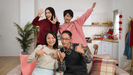 cheerful father. mother. adult daughter and son looking at camera and making thumb victory hand signs while taking burst shots at home during chinese spring festivalの写真素材