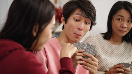 selective focus with closeup of son smiling slyly as the daughter looking at mother's eye gesture and drawing card. playing poker at home during spring festivalの写真素材