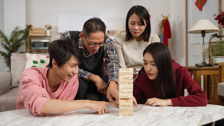 mother hitting father's hand to stop him and his son from affecting the player with finger pointing. daughter successfully removing and stacking the toy blockの写真素材