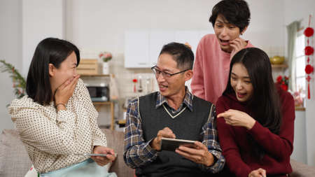 happy father cheering for victory on the mobile game with a thumb. family addictive to smartphone playing together on chinese lunar new year holiday at homeの写真素材