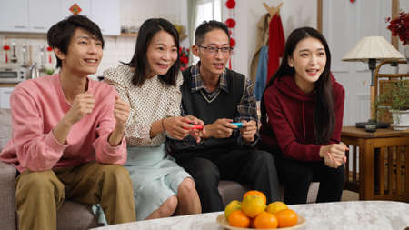 son and daughter cheering for their parents who are playing exciting racing game with joysticks in the living room at home during chinese lunar new year holidayの写真素材