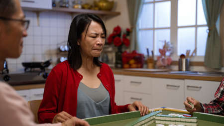 selective focus of mother winking at her son signaling him to pick the right tile while playing mahjong at home. gambling fraud in mahjong during chinese lunar new year conceptの写真素材