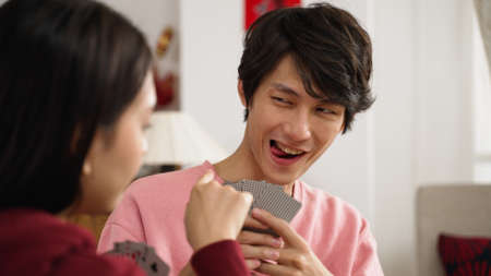 cunning son trying to affect his sister with funny face and feeling upset as she picks a good card. playing poker with family at home on chinese lunar new year holidayの写真素材