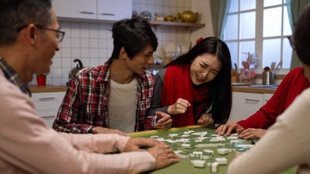 asian brother elbowed his sister out of chair while they are fighting at mahjong table. wagging finger refusing to give up. translation: luckの写真素材