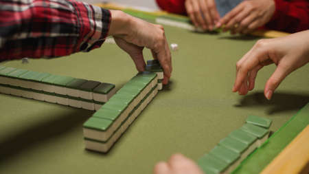 closeup with cropped view of player's hands taking turns picking two green tile stacks one by one at table while playing mahjong at homeの写真素材