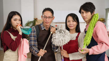 funny asian family of four showing up with cleaning tools in hands and smiling at camera on background of modern home kitchen with chinese lunar new year decorationsの写真素材