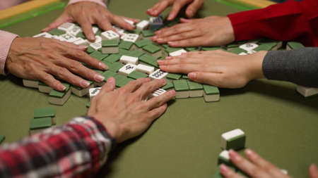 closeup view of hands mixing mahjong tiles on the table with green cloth. traditional asia gambling game during chinese lunar new year conceptの写真素材