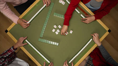 cropped top angle shot with of asian family taking turns drawing discarding tiles on green table while playing mahjong indoors during spring festival.の写真素材