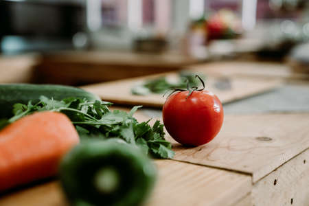 fresh vegetables ingredients for cooking on kitchen wooden counter. close up focus view on red tomato fruit on island table in home cooking place. diet healthy meal salad lifestyle concept.の写真素材