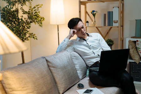 Young asian korean businessman working on laptop computer while sitting on sofa at home office....