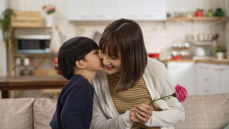 cute Asian boy giving a kiss on face and carnation flower to his mon on mother's day.の写真素材