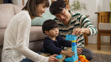happy japanese family of three enjoying playing plastic building blocks in the living room at home....