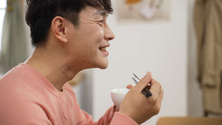 headshot with side view smiling asian man eating delicious food with bowl and chopsticks feeling...