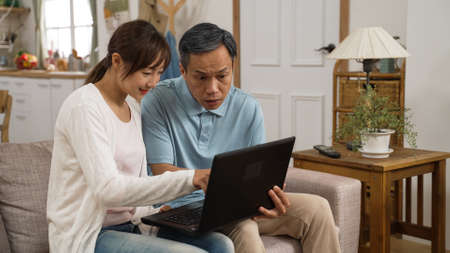 portrait of asian grandfather learning how to use laptop computer with adult granddaughterâ€™s...