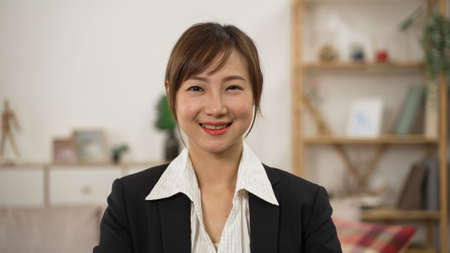 half length portrait of a professional pretty asian female insurance agent wearing suit and looking at camera. she smiles while posing at clientâs home backgroundの写真素材