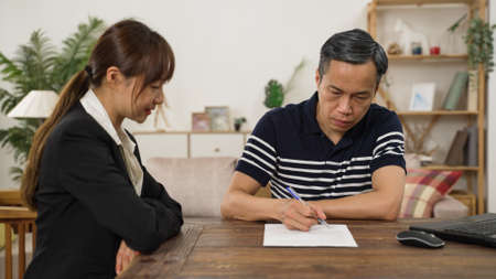 elderly man client putting signature on his disability insurance document after consultation at home. the female agent thanks him for the trustの写真素材