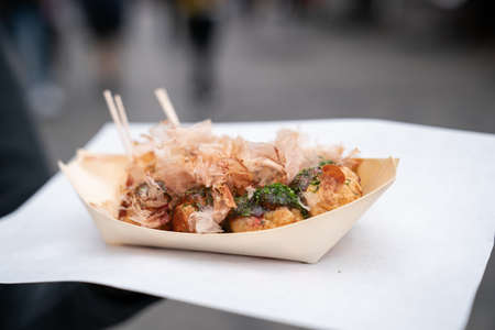 freshly cooked takoyaki ball-shaped octopus dumpling served in a paper tray with bonito flakes on...