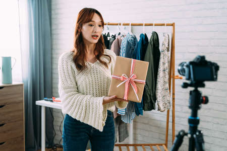 selective focus asian ecommerce business owner selling clothing is presenting a wrapped gift box in front of the camera while explaining campaign rule at home.の写真素材