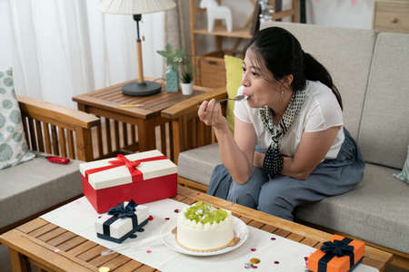 asian female celebrating birthday alone and indulging herself by having delicious cream cake in the...