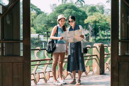 full length view from wooden door cheerful tourist girls are holding and reading a paper map...