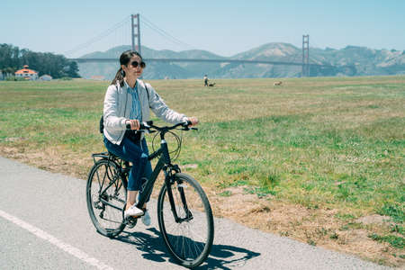 asian woman wearing sunglasses is having summer holiday fun by riding along a green field at leisure...
